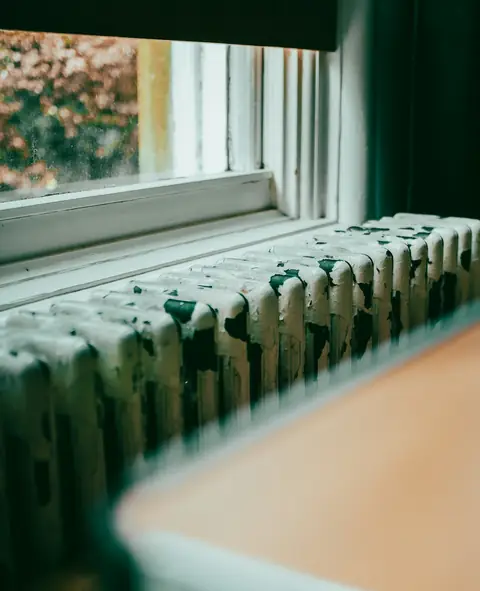 A cast-iron radiator under a window, with a blurred wooden sill in the foreground.